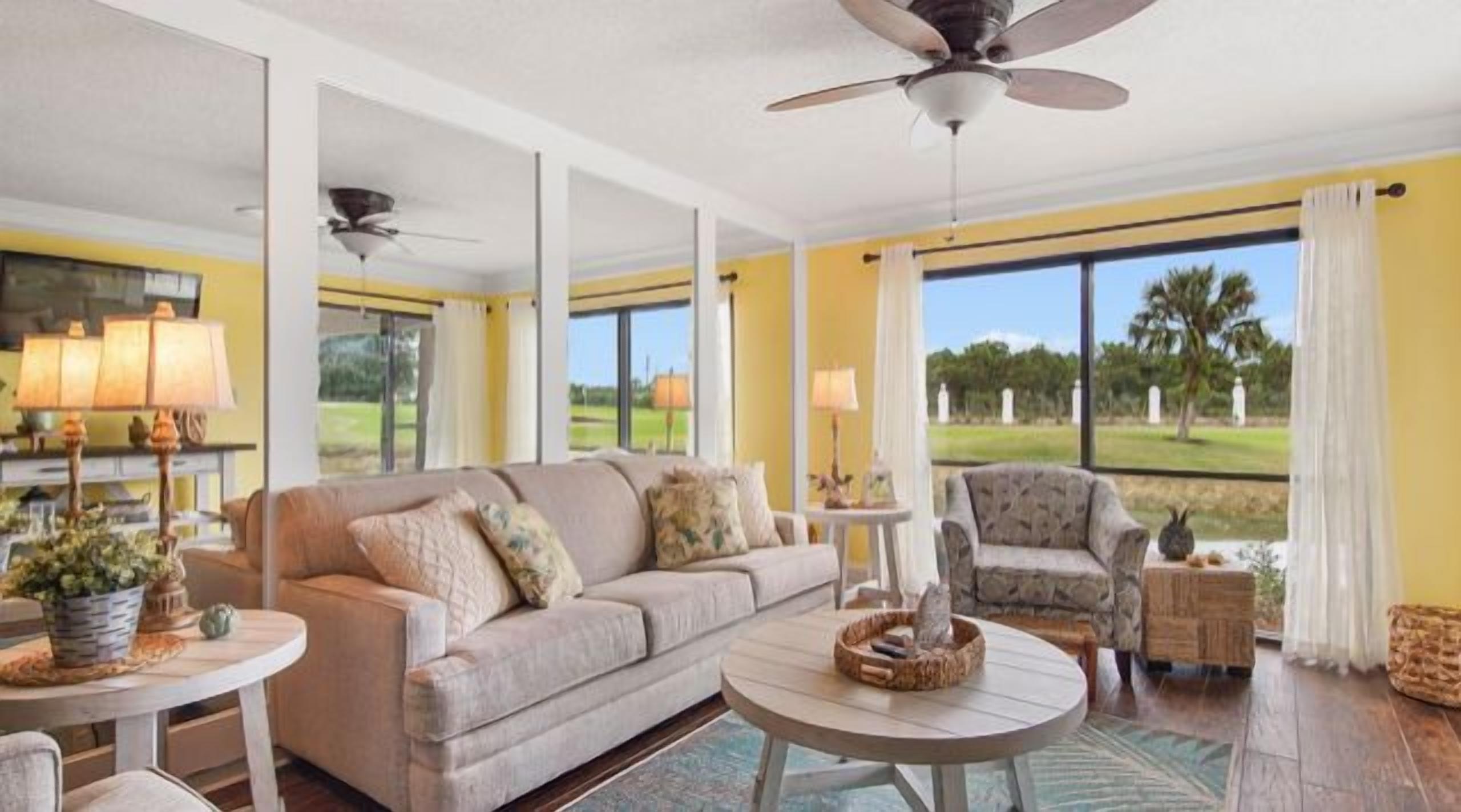 A spacious living room with a large window, a ceiling fan, and a round coffee table.