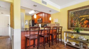 Una cocina con armarios de madera, una isla central con taburetes de bar, un microondas y un cuadro en la pared.