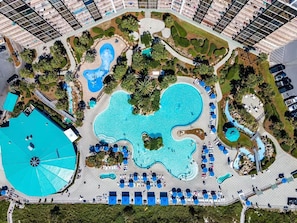Vista aérea de un resort con múltiples piscinas, tumbonas y palmeras.