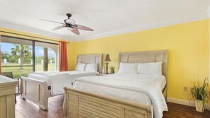 A hotel room with two beds, a ceiling fan, and a view of the outdoors.