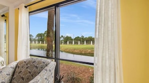 A room with a large window, a patterned chair, and a view of a water body and greenery.