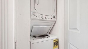 A compact, white, front-loading washing machine in a small laundry room with a door.