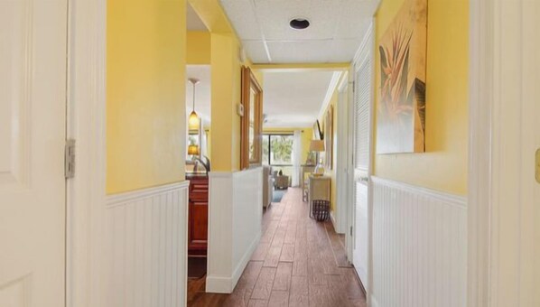 A hallway with a wooden floor, white wainscoting, and yellow walls.