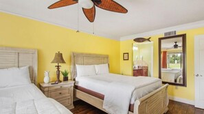 Habitación de hotel con dos camas, un ventilador de techo, una mesita de noche con lámpara y un espejo en la pared.