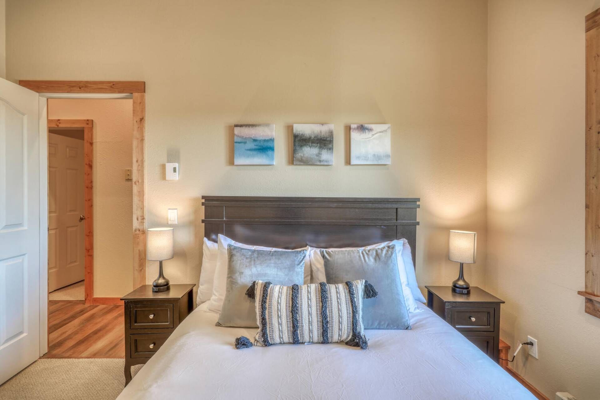 Een slaapkamer met een groot bed, twee nachtkastjes en drie aan de muur hangende schilderijen.