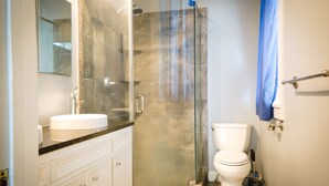 A modern bathroom with a glass-enclosed shower, a white toilet, and a sink with a marble countertop. - Arlington House (Natchez)