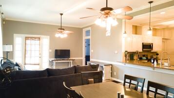 A modern kitchen with a dining area, a ceiling fan, and a television in the living room.