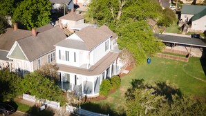 A two-story house with a porch, surrounded by a white picket fence, in a residential area. - Arlington House (Natchez)