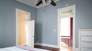 A bedroom with a bed, a dresser, and a ceiling fan. There are two doors, one leading to a balcony and another to a hallway. - Arlington House (Natchez)