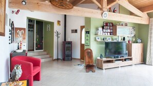 Una sala de estar con un sofá rojo, una silla de madera, un televisor y una estantería.