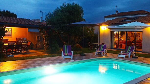 Una piscina con sillas de descanso y sombrillas, rodeada por un patio con suelo de baldosas.
