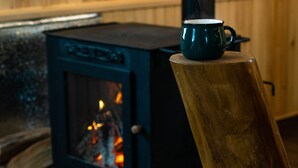 En brændeovn med synlig ild, en træskammel og et træbord med en kop.