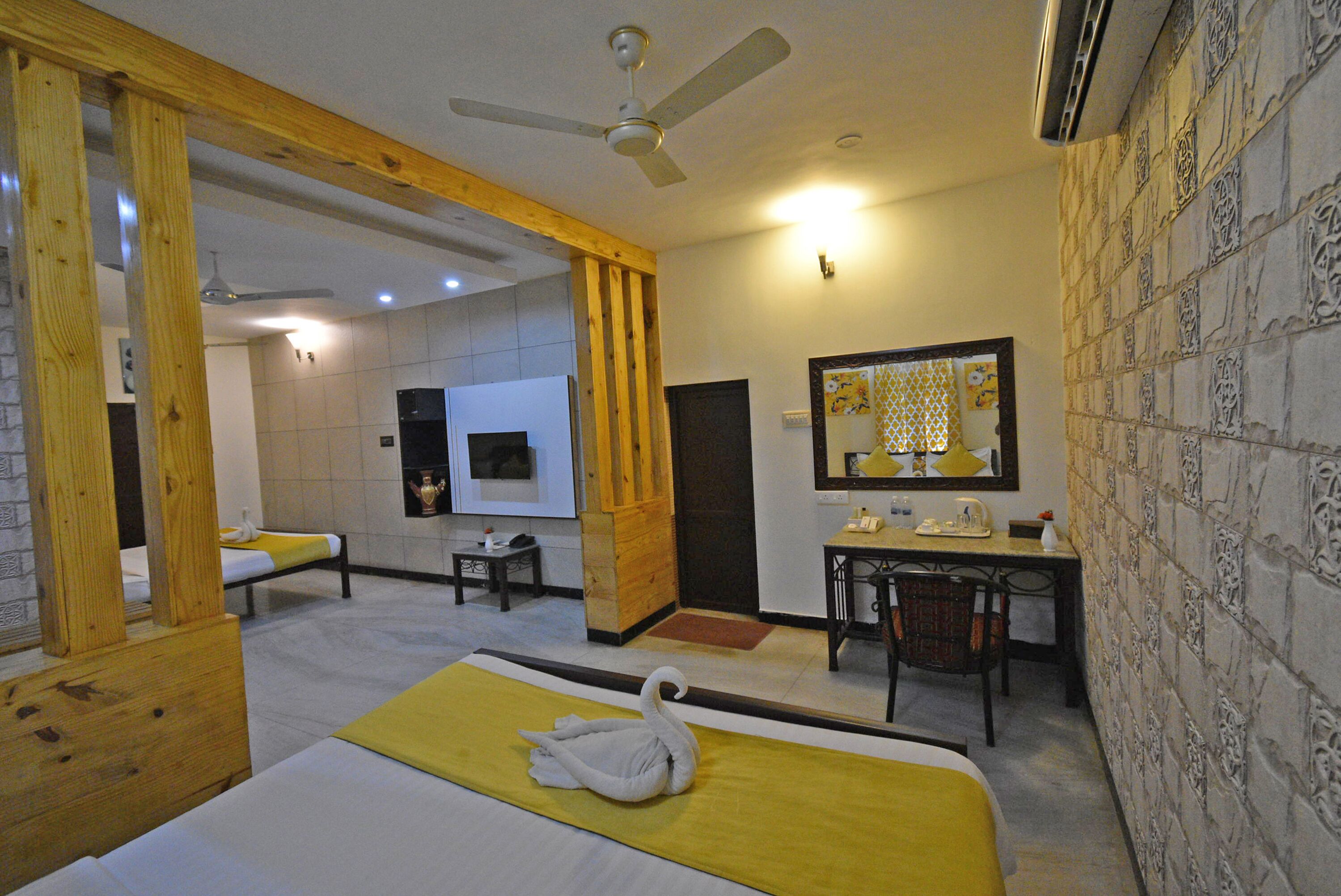 A hotel room with a bed, a desk, a chair, a mirror, and a ceiling fan.