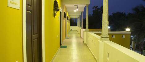 A hotel corridor with a yellow wall, a sign reading "Olive Blossom - 4", and a balcony with a railing.