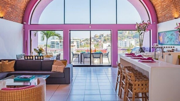 Un vaste espace de vie comprenant une grande fenêtre en arc de cercle, un canapé, une table basse et un coin repas avec des chaises et une table.
