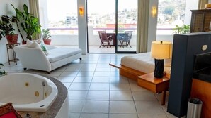 Une chambre d’hôtel avec un grand lit, un canapé, une petite table, une lampe, une baignoire et une vue sur la ville grâce à de grandes fenêtres.