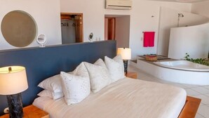 Une chambre à coucher comprenant un lit, une table de chevet, une lampe et donnant sur une salle de bain avec une baignoire et une douche.