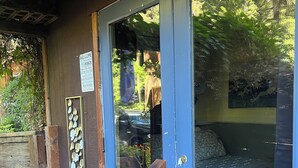 Een houten veranda met een blauwe deur die leidt naar een kamer met een kamerkleed met een patroon.