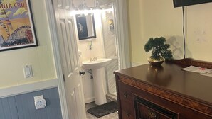Een badkamer met een wastafel, spiegel en douche. Er staat een houten dressoir met een televisie erboven.