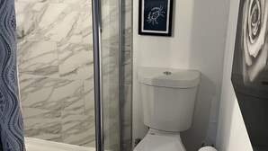 Een badkamer met een douchecabine van glas, een toilet en twee ingelijste foto’s aan de muur.