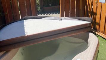 A hot tub with a wooden pergola overhead, surrounded by a wooden fence and greenery.