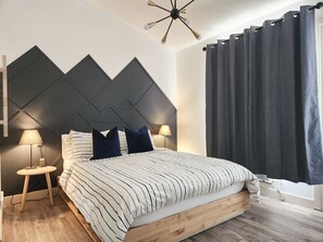 Un dormitori modern amb un llit, dues làmpades de nit, una làmpada de paret i una finestra amb cortines.
