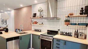 A modern kitchen with a dishwasher, stove, oven, and a sink. There are wooden cabinets and a countertop with various kitchen items. - The overlook stay | Free parking｜12 (Harvie Heights)