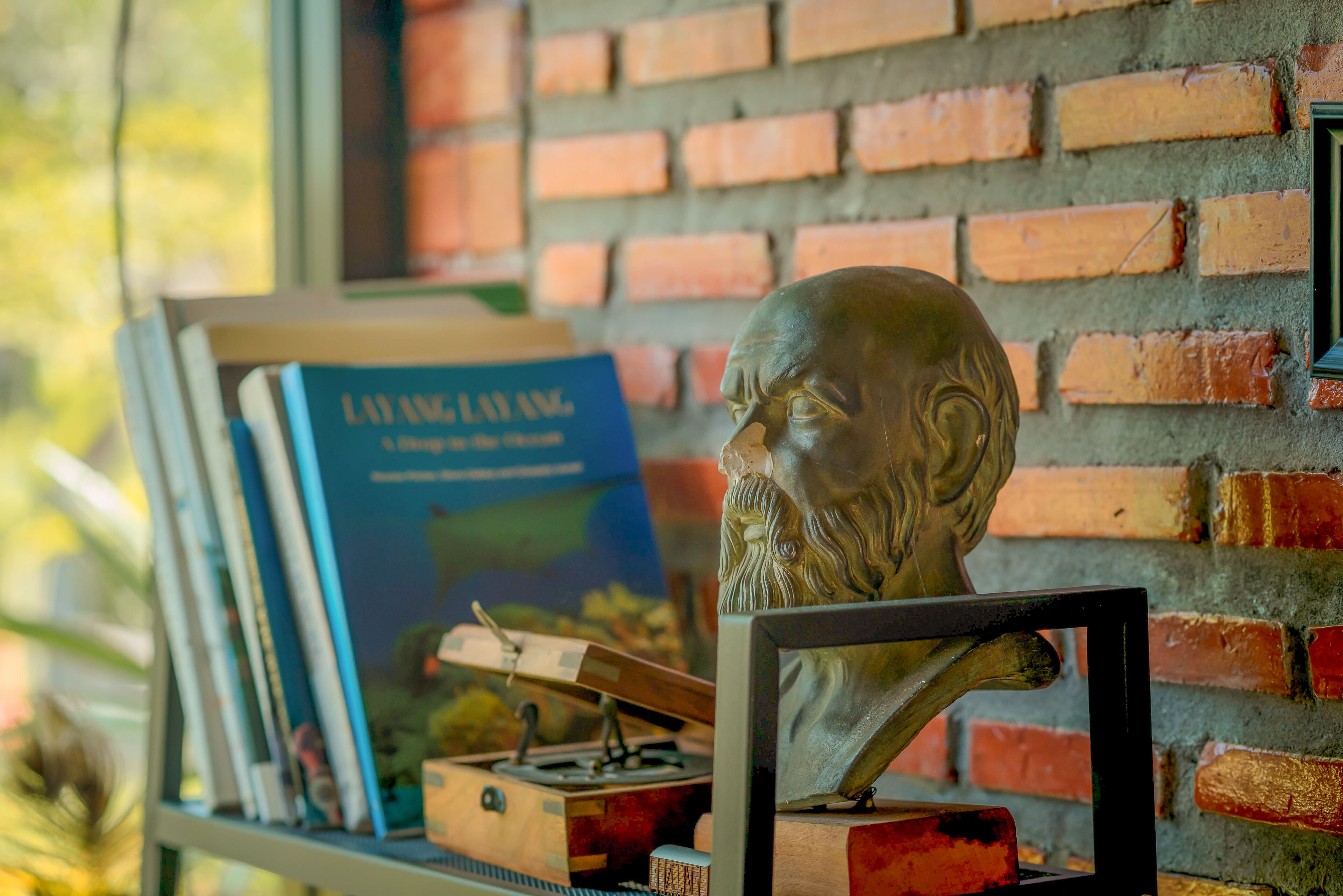 A brick wall, a bust sculpture, and a book titled "LAYANG LAYANG" on a shelf.