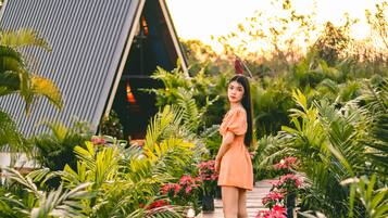 A woman in an orange dress standing on a wooden deck surrounded by lush greenery and a modern building structure.