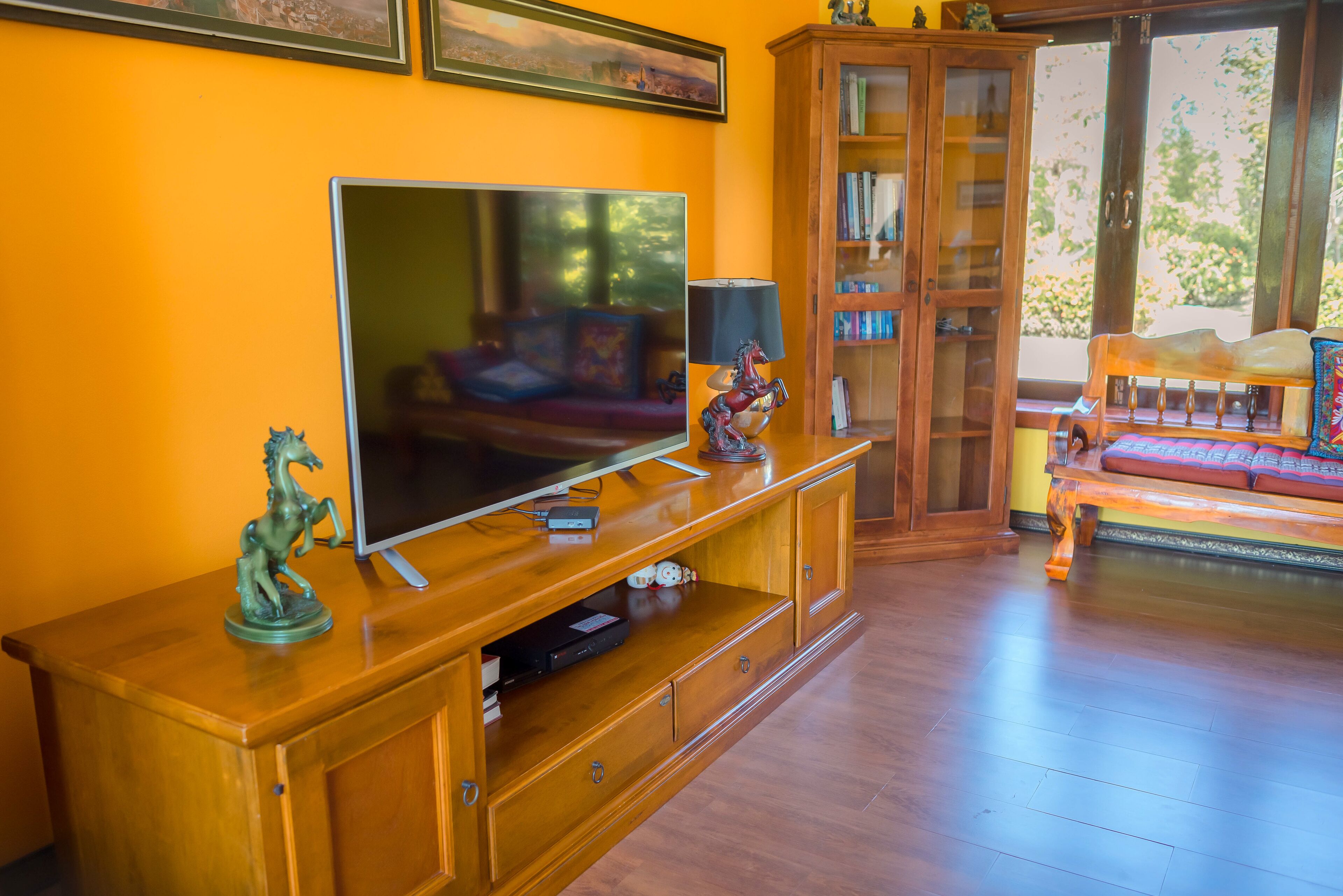 A living room with a wooden entertainment unit, a flat-screen TV, and a bookshelf.