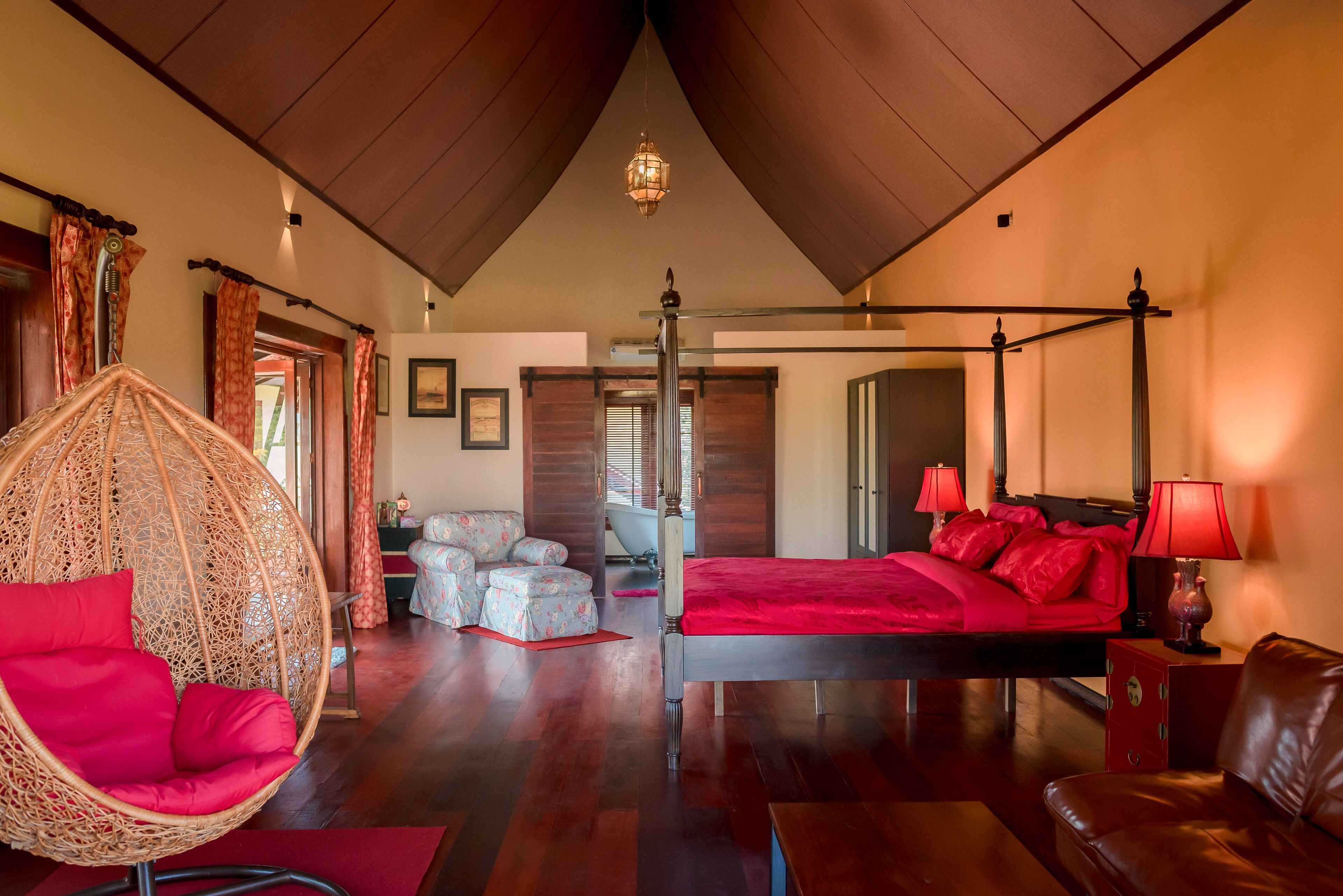 A spacious bedroom with a four-poster bed, a hanging chair, and a wooden ceiling.