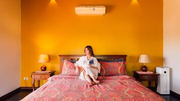 A bed with a patterned bedspread, two bedside lamps, a nightstand, a wall-mounted air conditioner, and a wall sconce.