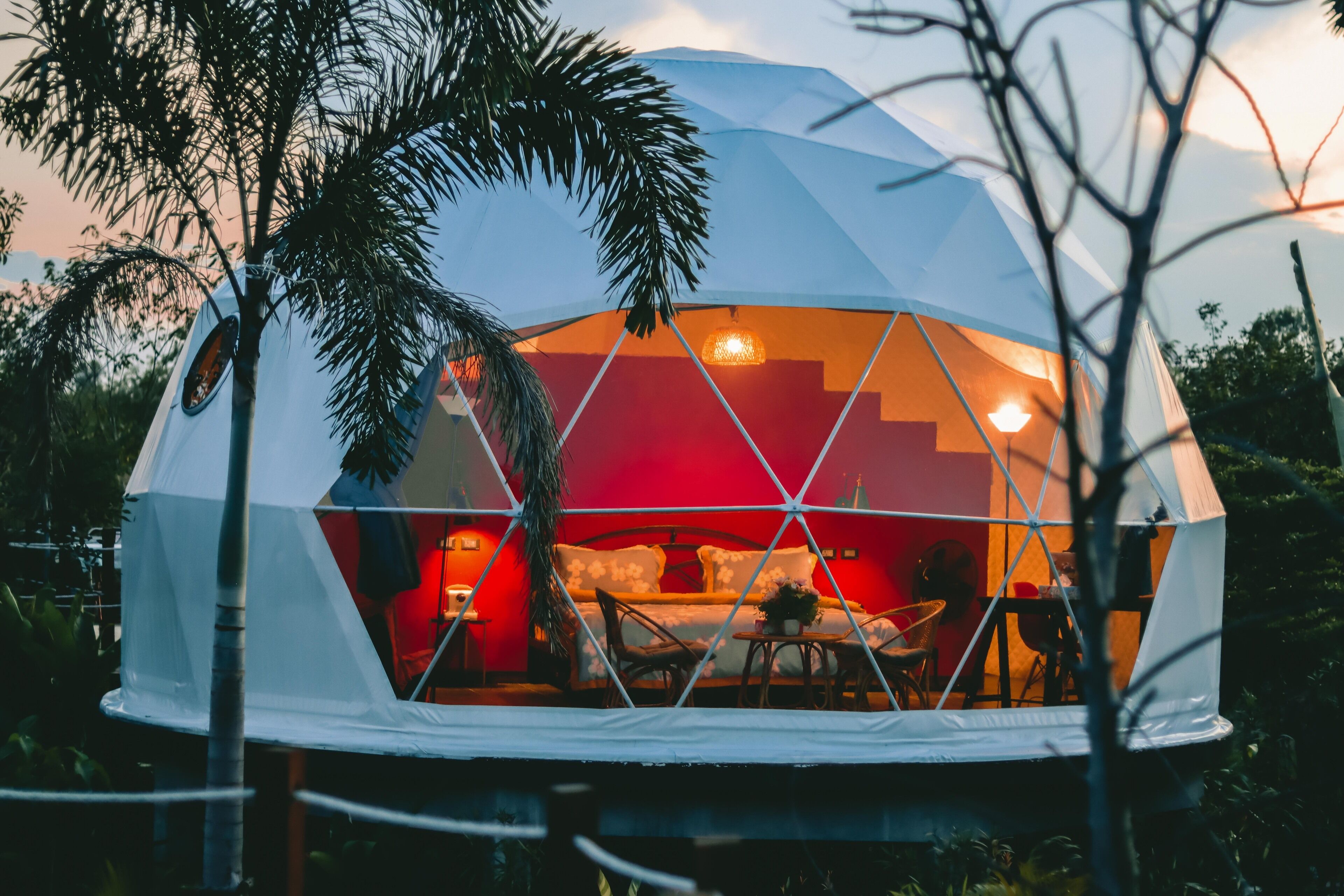 Una estructura en forma de cúpula geodésica con interior rojo, una cama y una mesa con sillas.