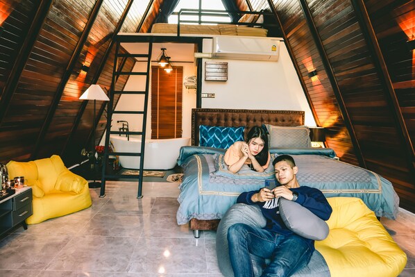 A cozy attic bedroom with a loft bed, a small desk, and a yellow bean bag.