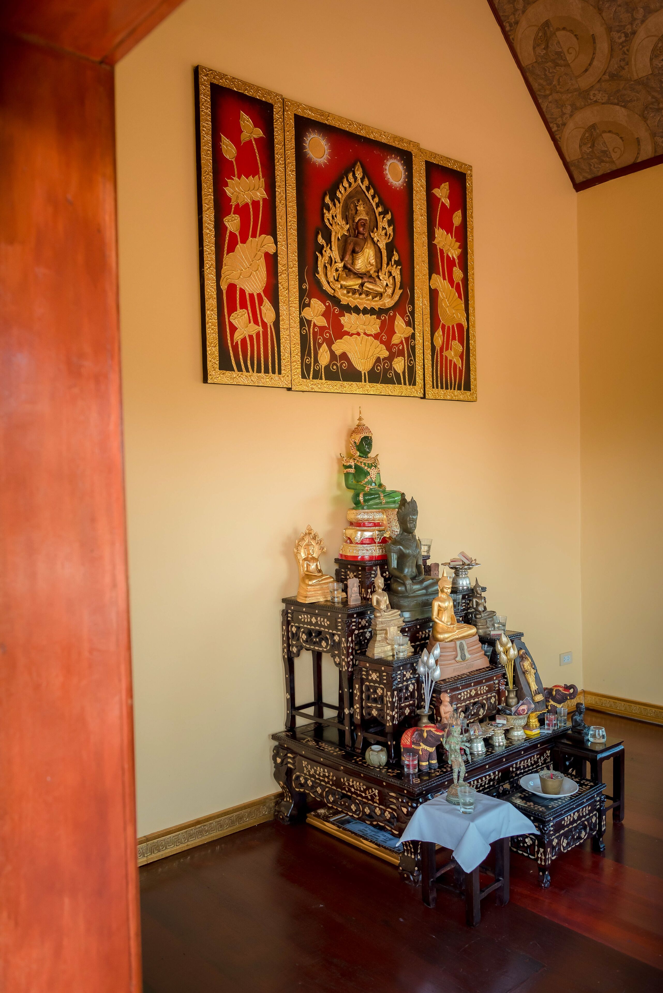 A room with a wooden floor, a wall-mounted shelf with statues and decorative items, and a ceiling with a patterned design.