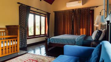 Un dormitorio con cama, cuna de madera, sofá azul, alfombra estampada y ventana con cortinas.