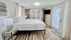 A bedroom with a bed, a bedside table, a TV mounted on the wall, and a door with a glass panel. - Charming 4/3 Lakehouse W/ Pool (Tampa)