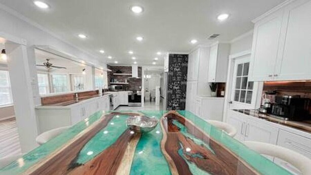 A modern kitchen with a central island, white cabinetry, and a unique wooden floor design. - Charming 4/3 Lakehouse W/ Pool (Tampa)