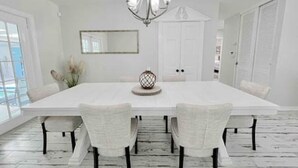 A spacious dining room with a white table, four chairs, a chandelier, and a large mirror on the wall. - Charming 4/3 Lakehouse W/ Pool (Tampa)