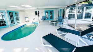 A modern indoor swimming pool with a clear blue pool, white walls, and blue doors. There are lounge chairs and a sunbed near the pool. - Charming 4/3 Lakehouse W/ Pool (Tampa)