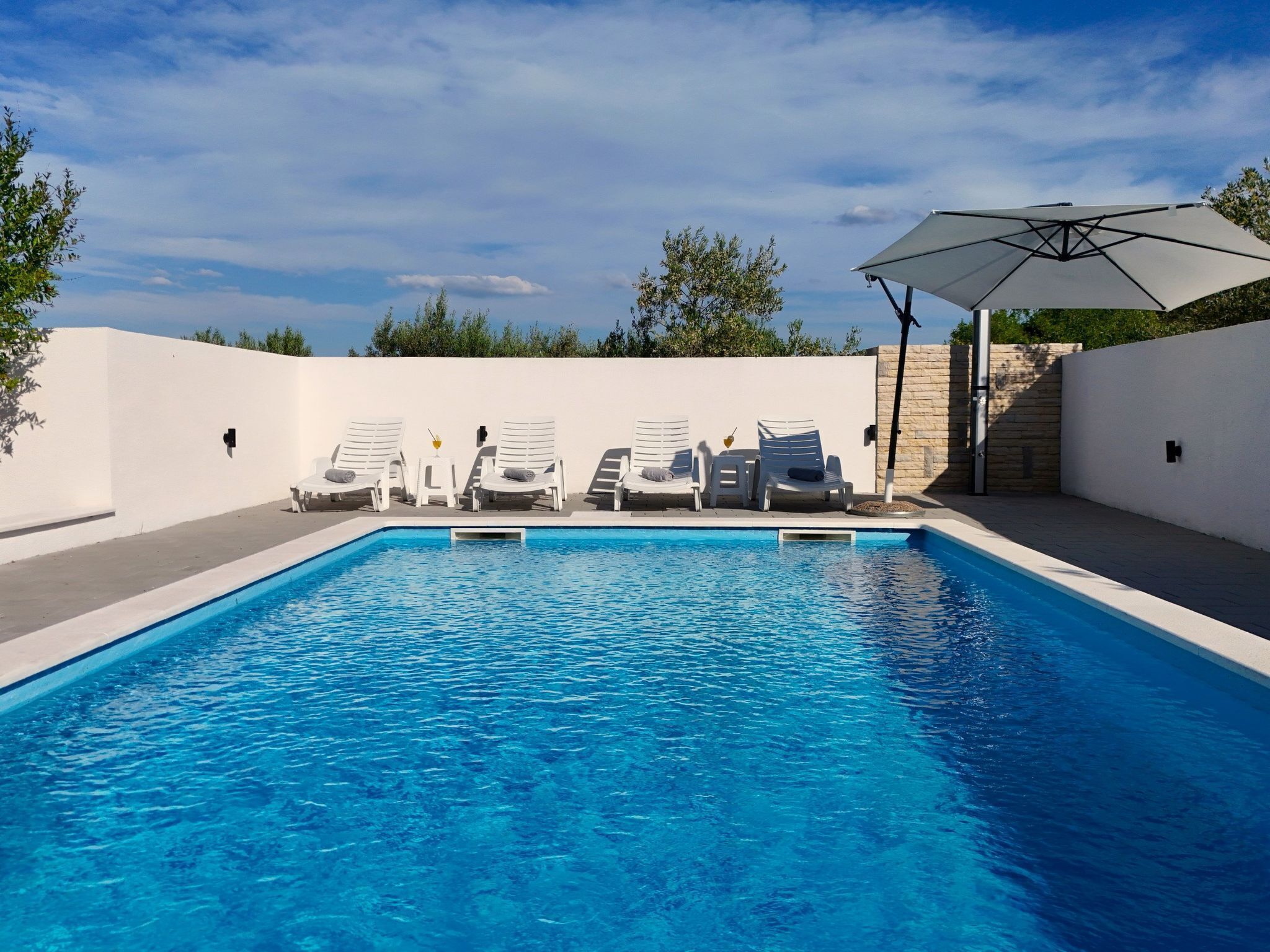 En swimmingpool med hvide liggestole og en hvid parasol.