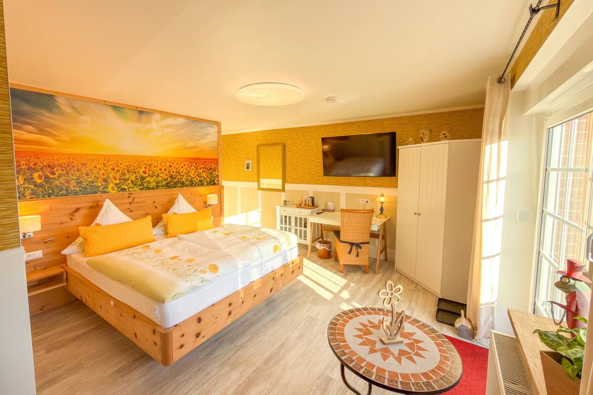 A bedroom with a bed, a desk, a chair, a TV, and a window.