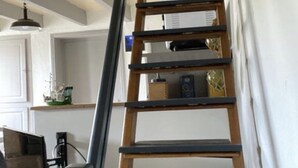 Un escalier intérieur en bois, doté d’une rampe, mène à un palier où se trouvent une étagère et une petite table.