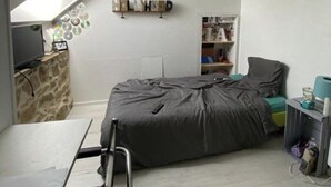 Une chambre à coucher de taille réduite, avec un plafond en pente, un lit, un petit bureau et une étagère contenant divers objets.