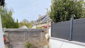 Une terrasse en bois avec une table et des chaises, entourée d’une clôture en bois et d’un mur blanc.