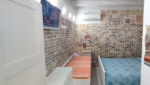 A small, enclosed room with a brick wall, a bed with a blue bedspread, a white cabinet, and a poster on the wall. - New LOFT on Ortigia waterfront for max 3 guests (siracusa)