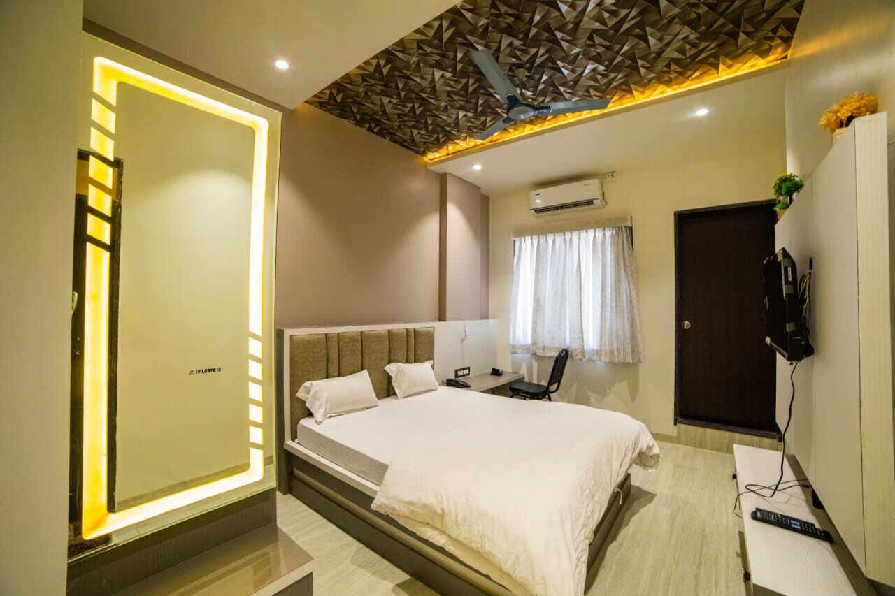 A modern hotel room with a bed, bedside table, chair, and a wall-mounted TV.