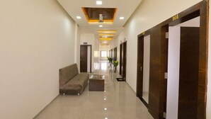 A hotel lobby with a long corridor, a sofa, a coffee table, and a reception desk. - Hotel KV Pride (Mehekar)