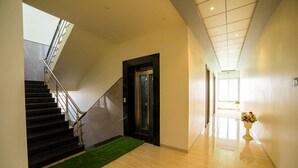 A modern hotel lobby with a staircase, a reception desk, and a hallway leading to the elevator. - Hotel KV Pride (Mehekar)