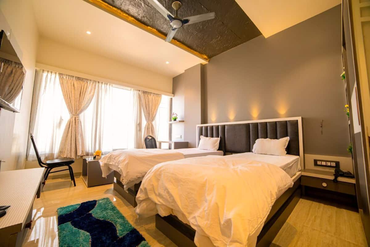 A hotel room with two beds, a desk, a chair, a ceiling fan, and a window with curtains.